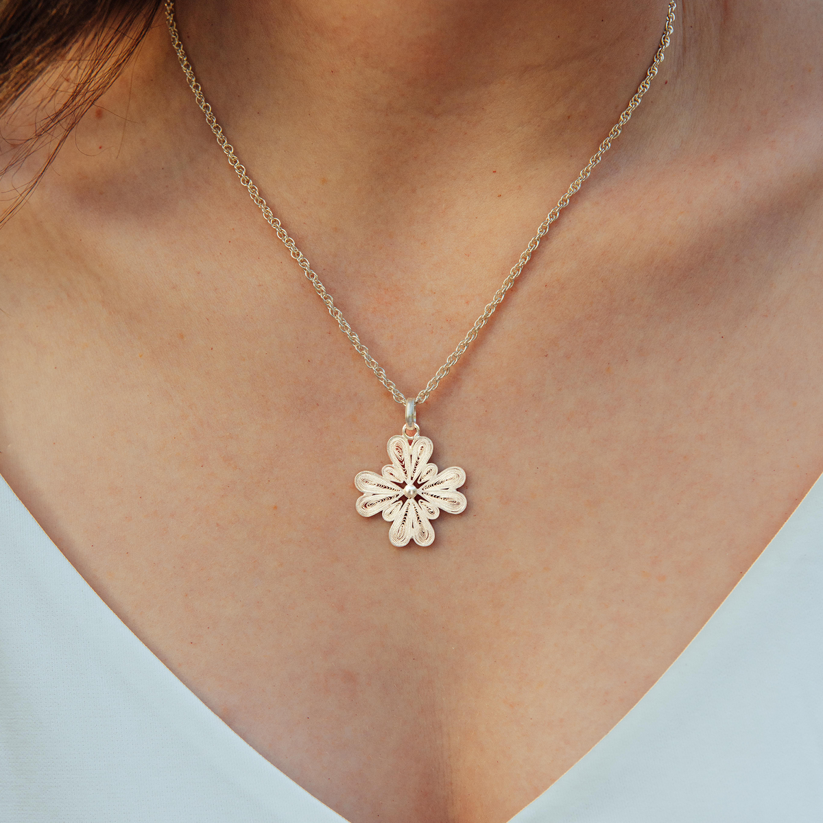 Close-up of a handmade 950 silver filigree flower pendant necklace by Oh Voila Jewelry, worn with a v-neck white top.