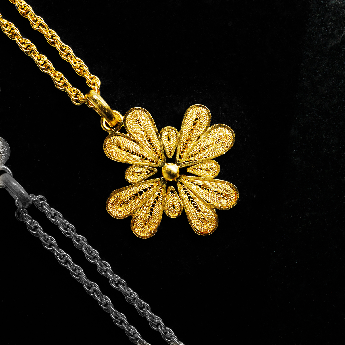 Close-up of handmade 18K gold vermeil filigree flower pendant necklace by Oh Voila Jewelry, shown on a black fabric background for contrast.


